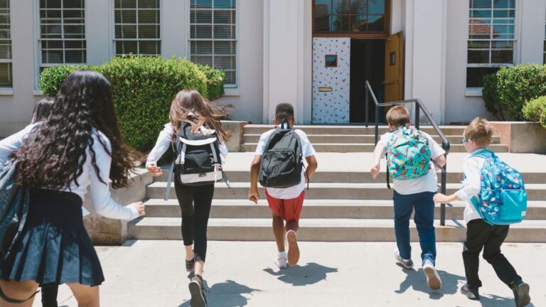 Children with backpacks running up stairs toward a school building, symbolizing back-to-school transitions. The image reflects the excitement and challenges, including anxiety, that can come with this time of year.