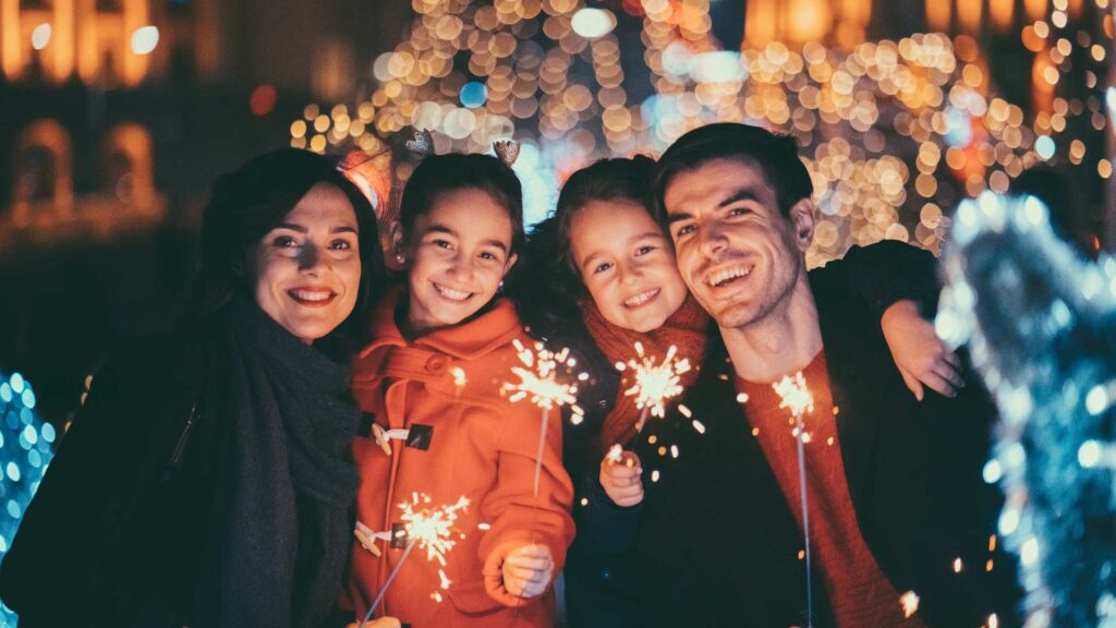 Family enjoying a quiet holiday evening with small sparklers and soft glowing lights, suggesting a peaceful and autism‑friendly celebration