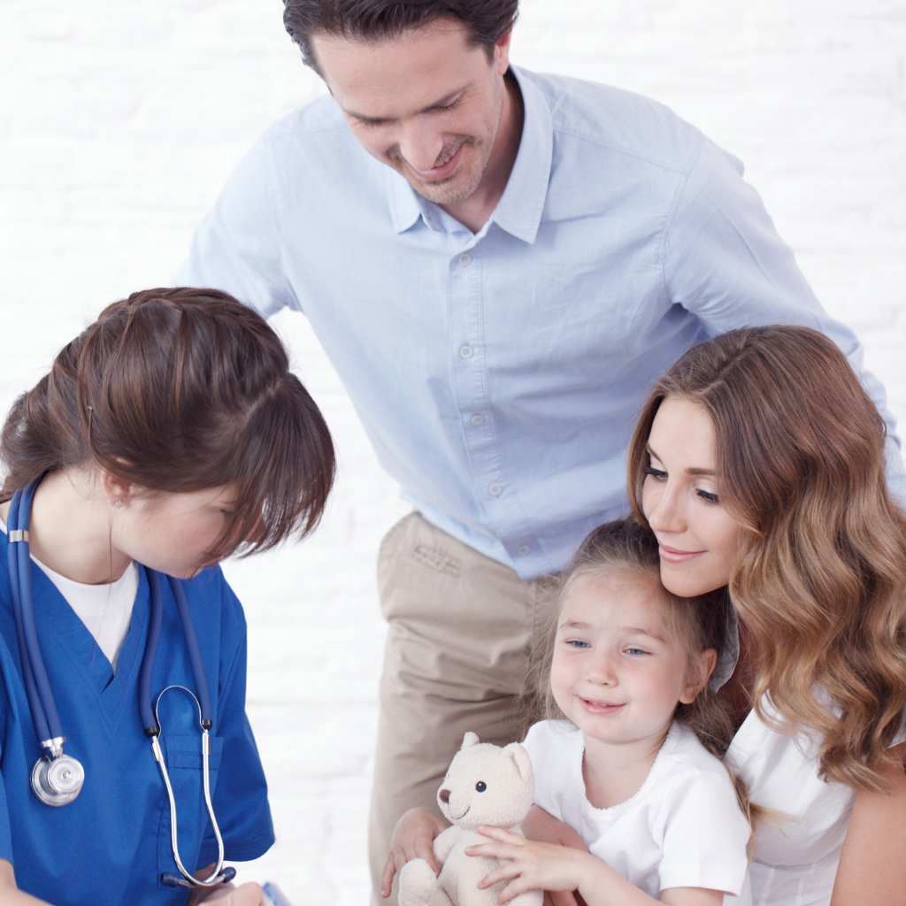 Pediatrician in teal scrubs examining a baby while parents look on during a medical checkup