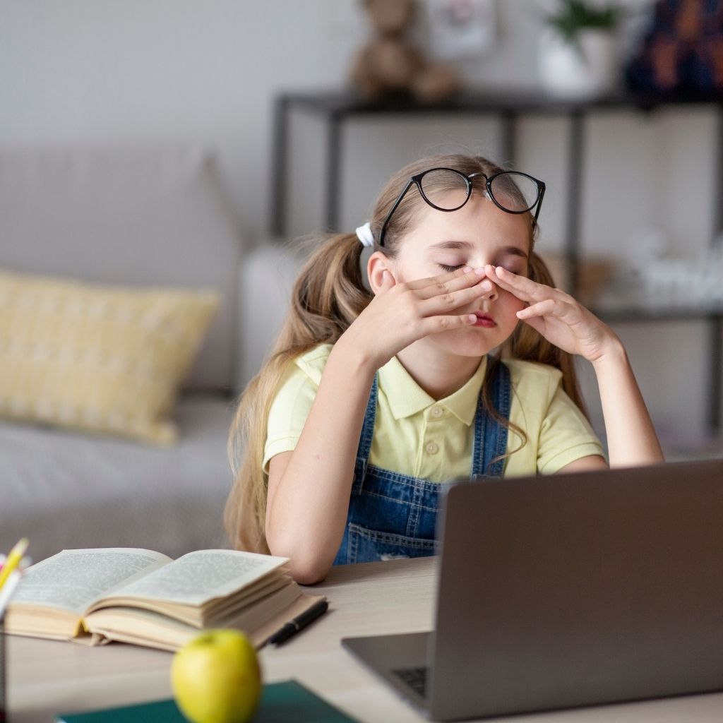 Child sitting at a desk with a laptop and schoolbook, experiencing back-to-school anxiety